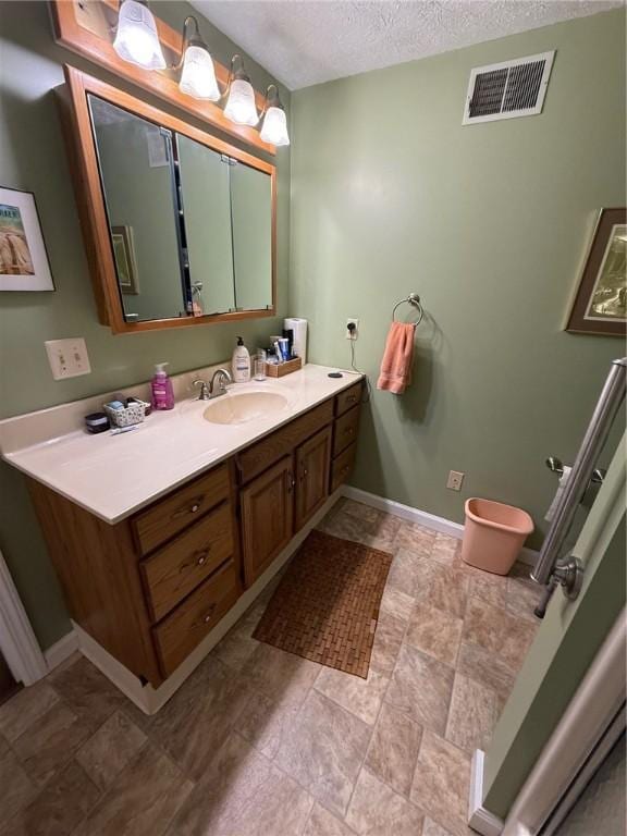 bathroom featuring vanity, a textured ceiling, baseboards, stone finish flooring, and visible vents