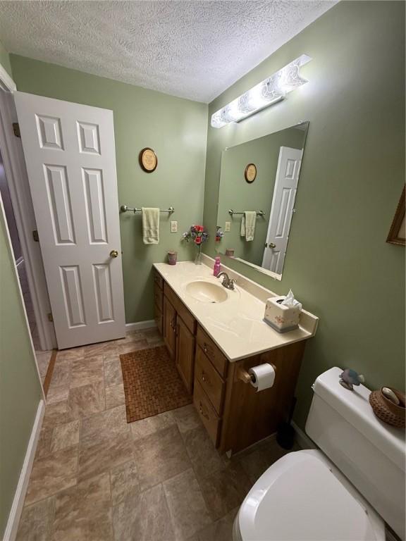bathroom featuring vanity, toilet, a textured ceiling, baseboards, and stone finish flooring