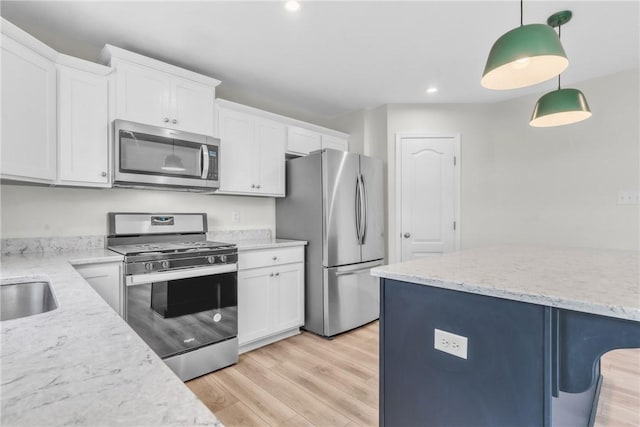 kitchen featuring light stone countertops, stainless steel appliances, light wood-style flooring, white cabinetry, and hanging light fixtures