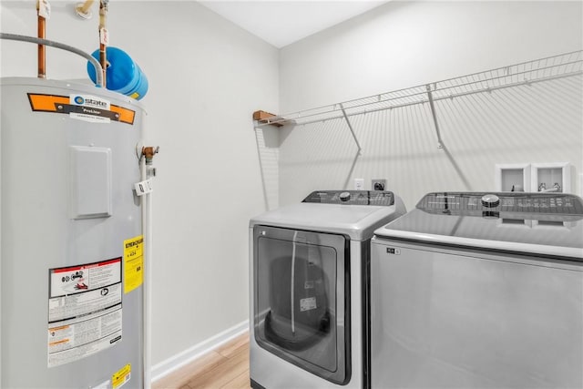 washroom featuring laundry area, electric water heater, light wood-style floors, washing machine and dryer, and baseboards