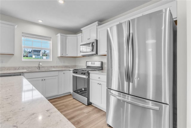 kitchen featuring light wood finished floors, recessed lighting, a sink, white cabinetry, and appliances with stainless steel finishes