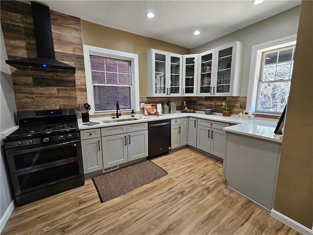 kitchen featuring black dishwasher, extractor fan, light wood-type flooring, range with two ovens, and a sink