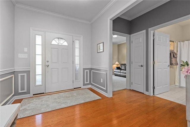 entrance foyer featuring wood finished floors, a wainscoted wall, and ornamental molding