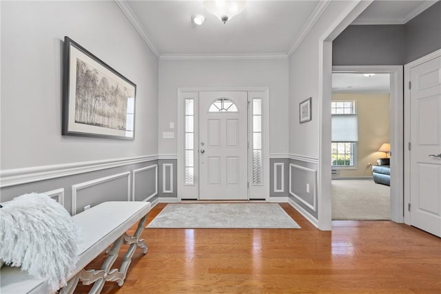 entrance foyer featuring wood finished floors, ornamental molding, and wainscoting