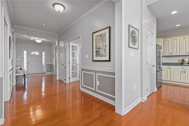 hall featuring crown molding, wainscoting, light wood-style flooring, and a decorative wall