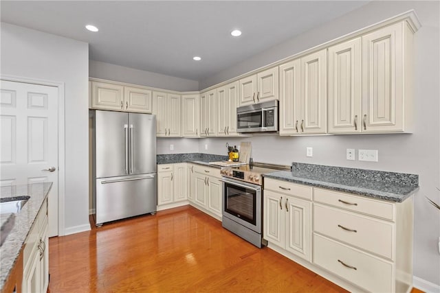 kitchen featuring light wood finished floors, recessed lighting, dark stone countertops, and appliances with stainless steel finishes