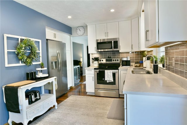 kitchen featuring tasteful backsplash, stainless steel appliances, light countertops, white cabinets, and a sink