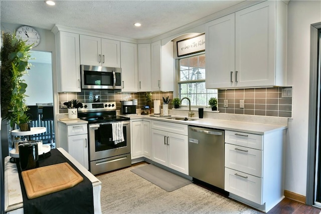 kitchen with stainless steel appliances, light countertops, white cabinets, backsplash, and a sink