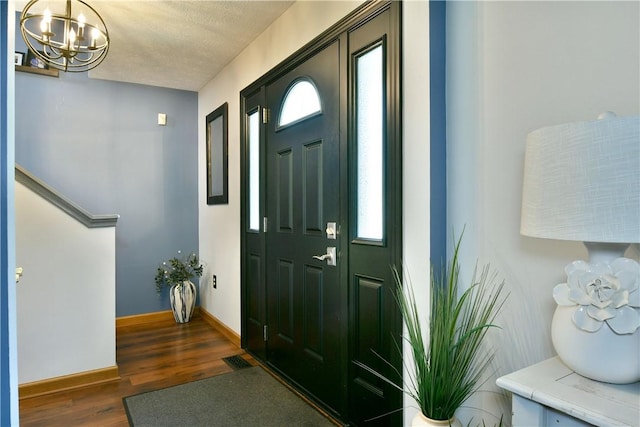 entryway with a textured ceiling, wood finished floors, a chandelier, and baseboards