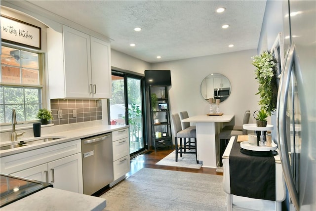 kitchen featuring a textured ceiling, white cabinets, a sink, appliances with stainless steel finishes, and recessed lighting