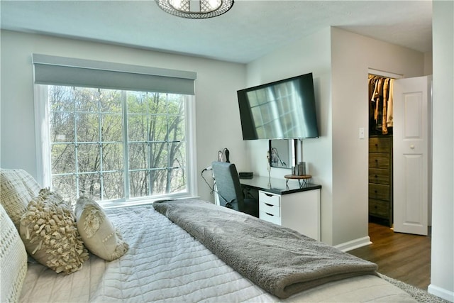 bedroom featuring baseboards, wood finished floors, and a walk in closet