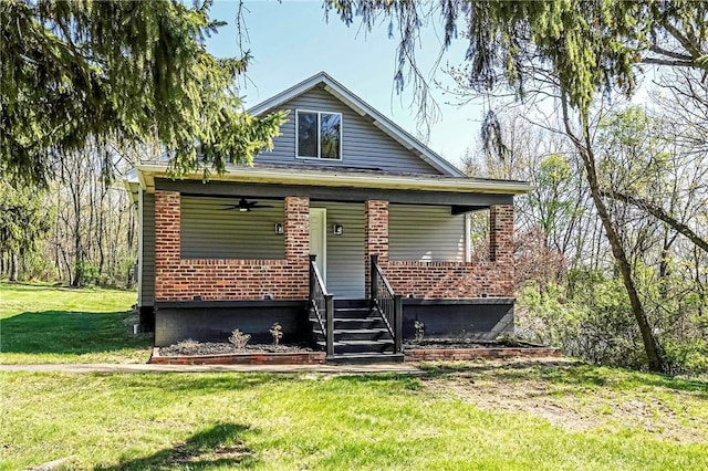 bungalow featuring brick siding, a porch, ceiling fan, and a front yard