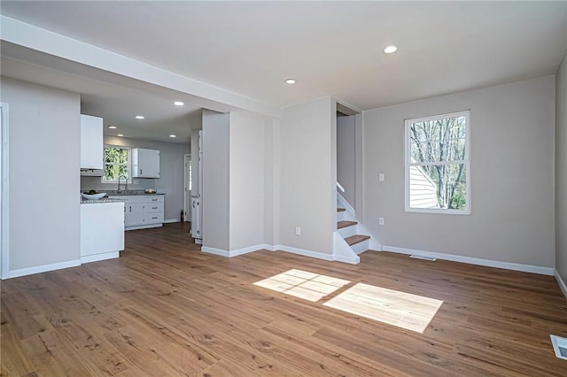 unfurnished living room with baseboards, stairway, wood finished floors, and a sink