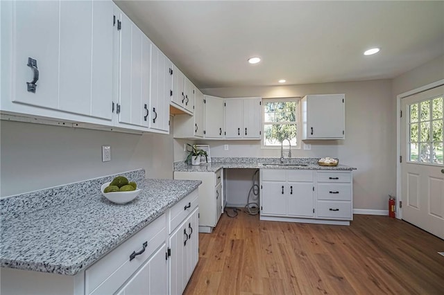 kitchen featuring light wood finished floors, a sink, white cabinets, and light stone counters
