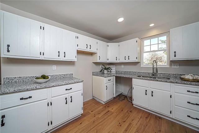 kitchen featuring light stone counters, white cabinetry, a sink, light wood-type flooring, and recessed lighting