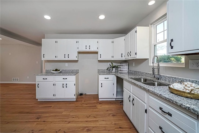 kitchen featuring light stone counters, white cabinetry, recessed lighting, and a sink