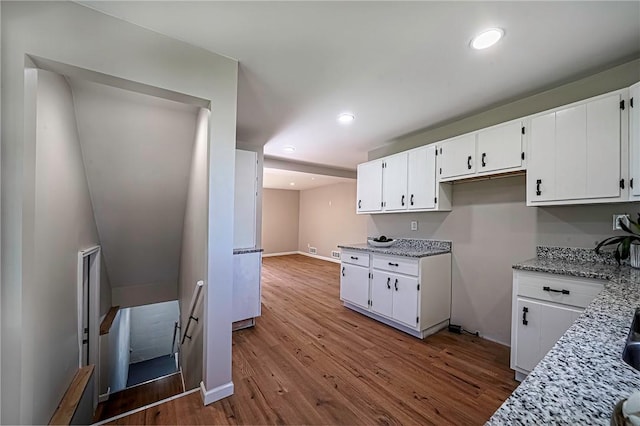 kitchen featuring recessed lighting, light stone countertops, white cabinetry, baseboards, and wood finished floors