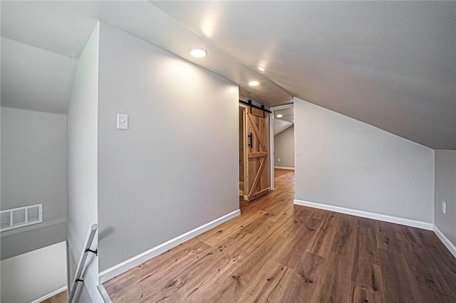 bonus room with visible vents, a barn door, recessed lighting, vaulted ceiling, and wood finished floors
