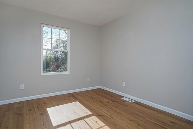 unfurnished room with wood finished floors, visible vents, and baseboards