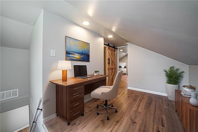 office with a barn door, visible vents, vaulted ceiling, and light wood-style floors