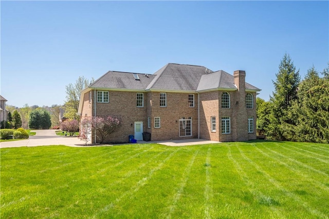 back of house with a chimney, brick siding, a patio area, and a lawn