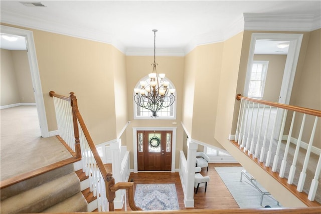 foyer featuring an inviting chandelier, crown molding, visible vents, baseboards, and wood finished floors