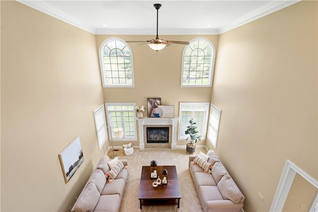 carpeted living area with a towering ceiling, ceiling fan, a high end fireplace, and plenty of natural light