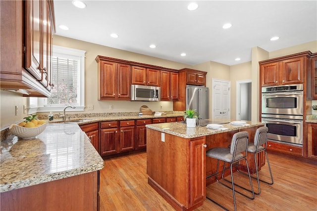 kitchen featuring a sink, stainless steel appliances, light stone counters, light wood-style flooring, and a kitchen island