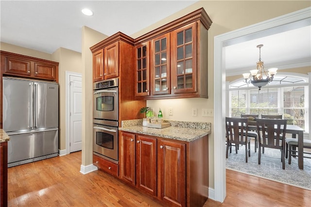kitchen with stainless steel appliances, a notable chandelier, glass insert cabinets, and light wood-style flooring
