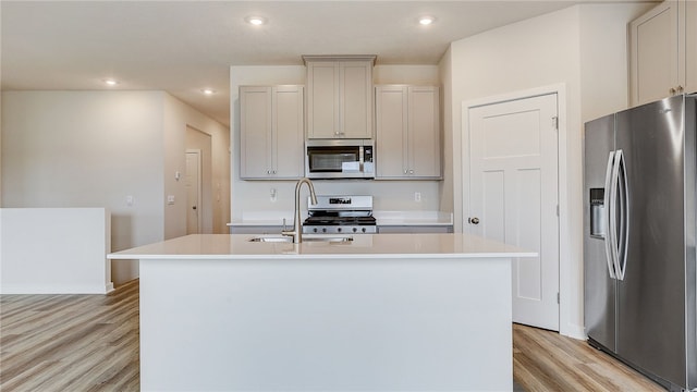 kitchen with light wood-style flooring, a sink, appliances with stainless steel finishes, light countertops, and an island with sink