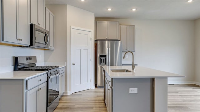 kitchen with a sink, light wood-style flooring, gray cabinetry, appliances with stainless steel finishes, and an island with sink