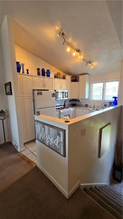 kitchen with white cabinets, light countertops, vaulted ceiling, track lighting, and white appliances