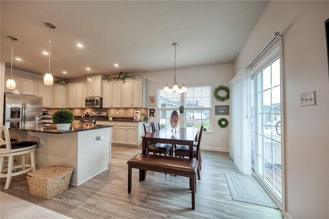 kitchen with a breakfast bar area, light wood finished floors, backsplash, a notable chandelier, and appliances with stainless steel finishes