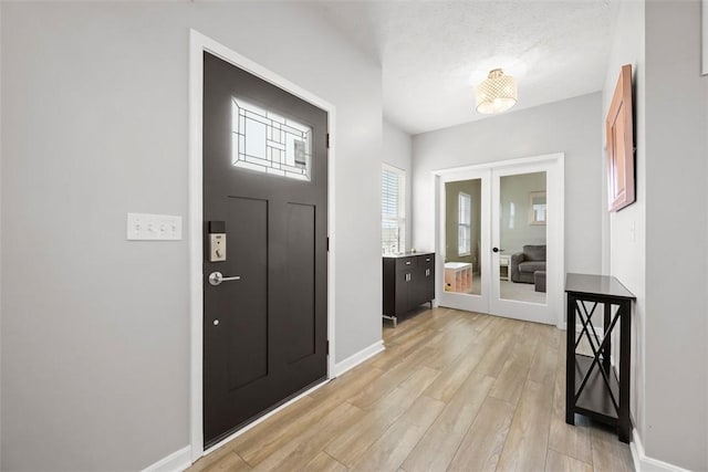 entryway with light wood finished floors, french doors, and baseboards