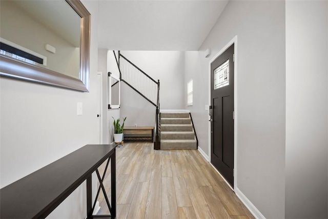 foyer with baseboards, stairway, and light wood-style flooring