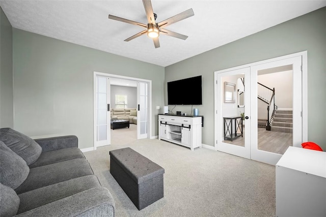 living area with stairway, ceiling fan, light colored carpet, baseboards, and french doors