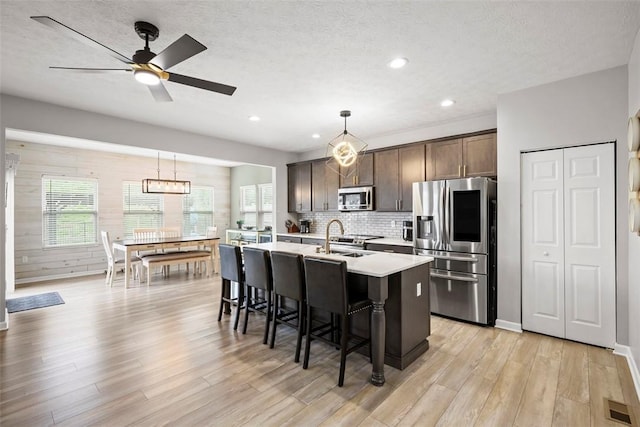 kitchen featuring visible vents, stainless steel appliances, dark brown cabinetry, light wood finished floors, and a center island with sink