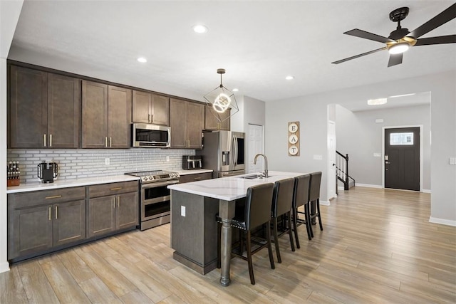 kitchen featuring a sink, stainless steel appliances, a kitchen breakfast bar, light wood-style flooring, and backsplash
