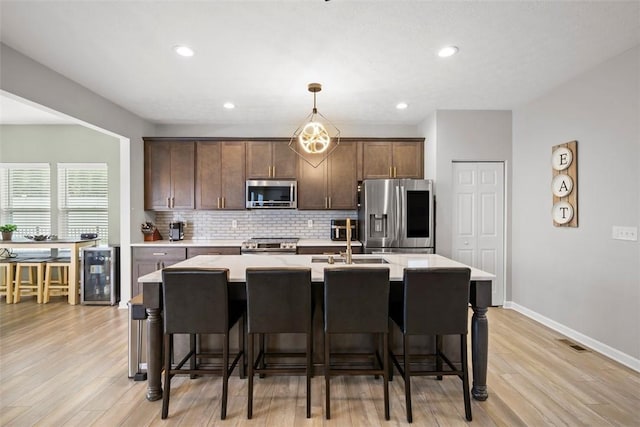 kitchen featuring a sink, decorative backsplash, wine cooler, a center island with sink, and appliances with stainless steel finishes