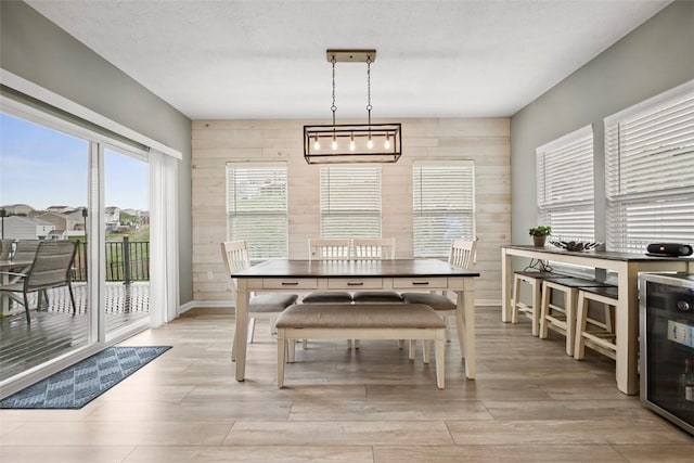 dining room featuring baseboards, wooden walls, light wood-style flooring, and wine cooler