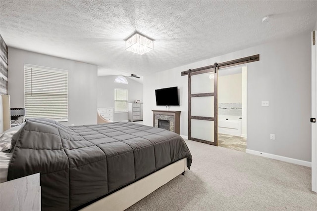 carpeted bedroom featuring a textured ceiling, baseboards, a barn door, and ensuite bathroom