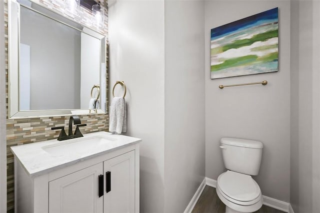 half bath featuring vanity, decorative backsplash, toilet, baseboards, and wood finished floors