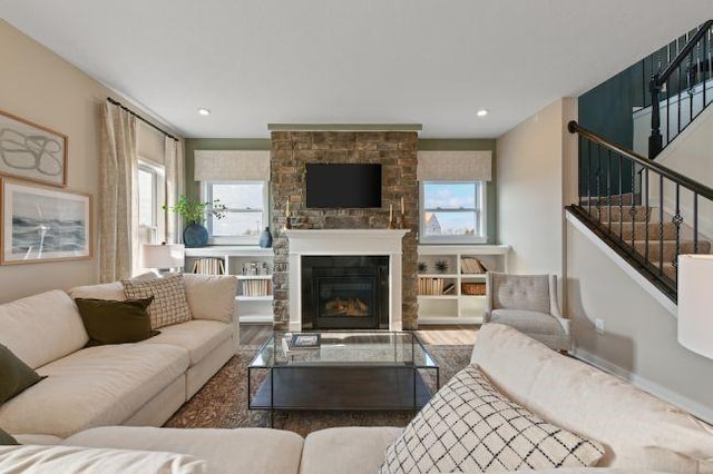 living area with a glass covered fireplace, stairway, wood finished floors, and a healthy amount of sunlight
