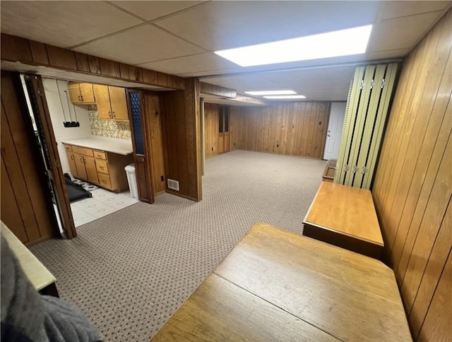 finished basement featuring wooden walls, visible vents, a drop ceiling, and light carpet