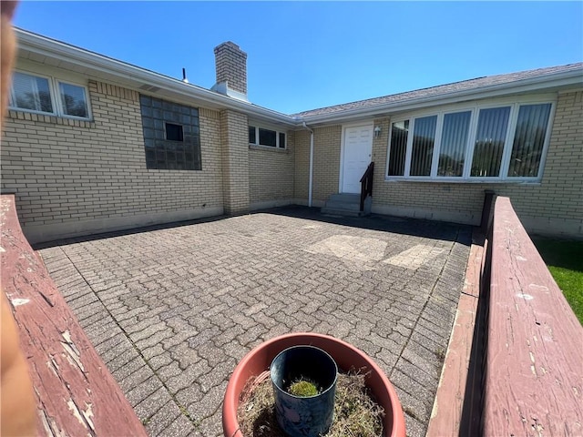rear view of property featuring a chimney, brick siding, a patio, and entry steps
