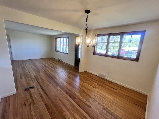 unfurnished dining area with an inviting chandelier, baseboards, wood finished floors, and visible vents