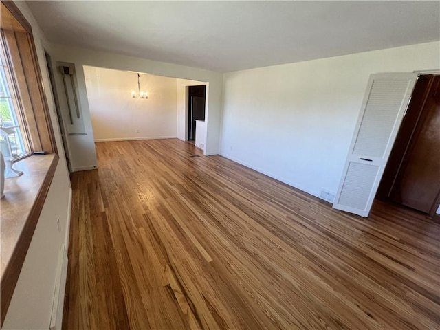 unfurnished living room featuring a notable chandelier, wood finished floors, and baseboards