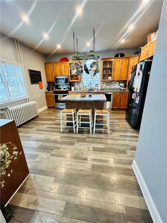 kitchen featuring stainless steel appliances, light wood-style floors, a kitchen breakfast bar, a center island, and backsplash