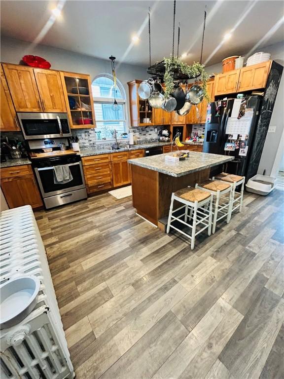 kitchen with a breakfast bar area, decorative backsplash, light wood-style floors, black appliances, and brown cabinetry