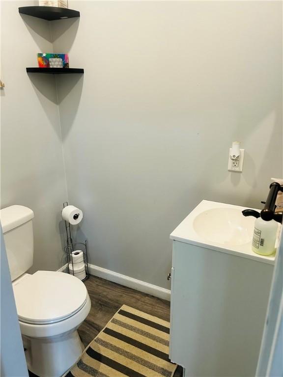 bathroom with toilet, vanity, wood finished floors, and baseboards